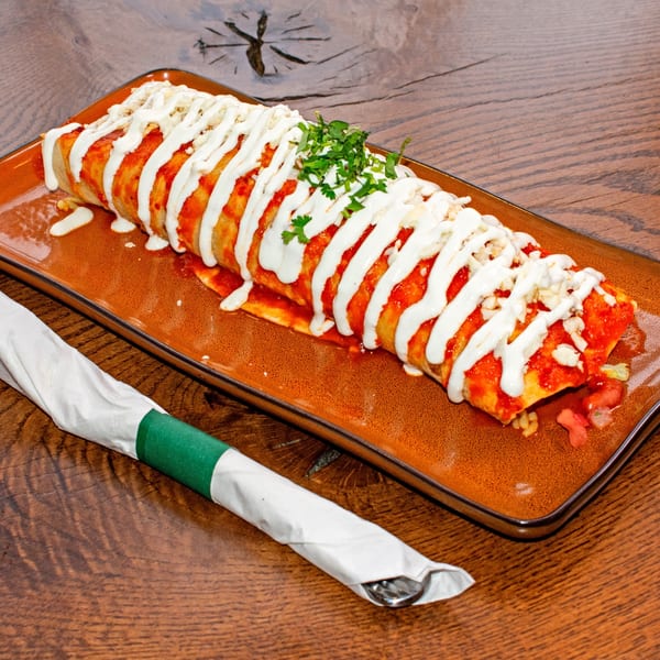 A large, saucy burrito topped with sour cream, cheese, and cilantro on a brown plate.