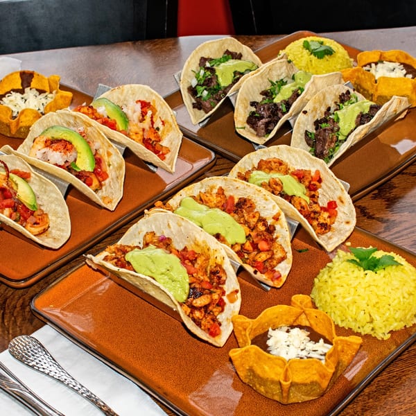 Assortment of Orale Mexican Restaurant tacos, including steak, shrimp, and chicken, with rice and bean cups.